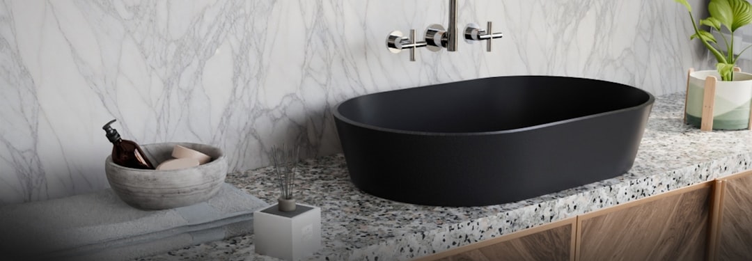 services-04 A sophisticated matte-black oval washbasin rests on a textured stone countertop, complemented by a wall-mounted chrome faucet. The white marble backsplash, warm wooden cabinetry, and subtle décor accents create a balanced blend of luxury, minimalism, and contemporary design, perfect for high-end modern bathrooms.